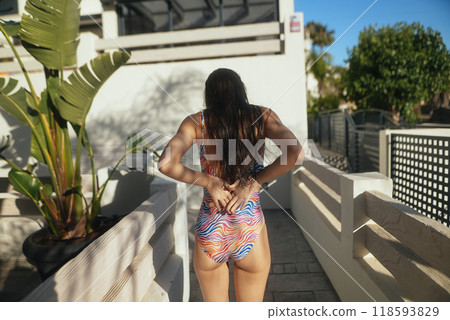 A woman wearing a colorful and stylish swimsuit happily walking outdoors at the beach 118593829