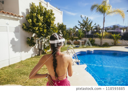 A Young Woman Relaxing by the Pool in a Beautiful Summer Setting While Wearing a VR Headset 118593885