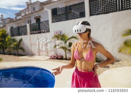 A young woman is enjoying a vibrant virtual reality experience while relaxing by the pool, A young woman is enjoying a vibrant virtual reality experience while relaxing by the pool, 118593893