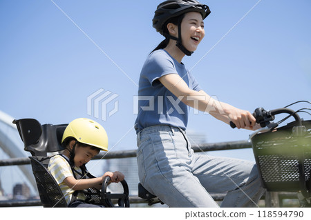Mom and child riding bicycles on a beautiful road under blue sky. Going out or going to work on a mamachari. Upper body. Mom and child riding bicycles on a beautiful road under blue sky. Going out or going to work on a mamachari. Upper body. 118594790