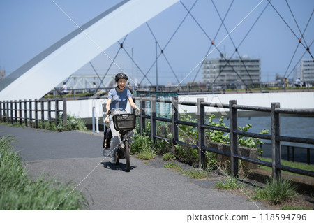 Mom and child riding bicycles on a beautiful road with blue sky. Going out or going to work on a mamachari. Wide-angle shot of the whole body. Greenery is blurred in front. Mom and child riding bicycles on a beautiful road with blue sky. Going out or going to work on a mamachari. Wide-angle shot of the whole body. Greenery is blurred in front. 118594796