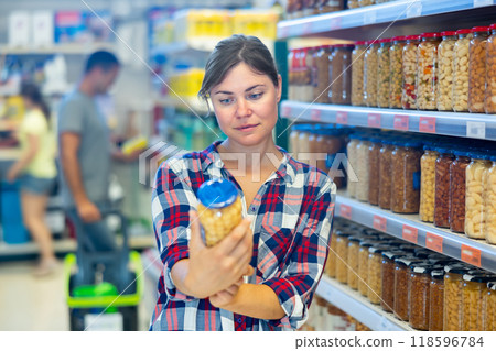 Female shopper choosing canned pickled vegetables in supermarket Female shopper choosing canned pickled vegetables in supermarket 118596784