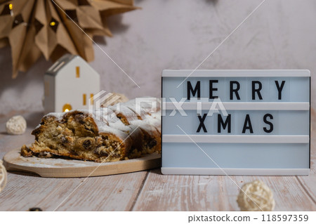 Lightbox with saying MERRY XMAS. Traditional German Christmas stollen cake in background of handmade festive decor. Winter holiday treats. Vegan baking recipe Lightbox with saying MERRY XMAS. Traditional German Christmas stollen cake in background of handmade festive decor. Winter holiday treats. Vegan baking recipe 118597359