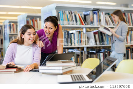 Two surprised female colleagues working on join project in library 118597608