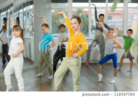 Positive juvenile girl engaged in Rock 'n' Roll dance in training room with children's group 118597769