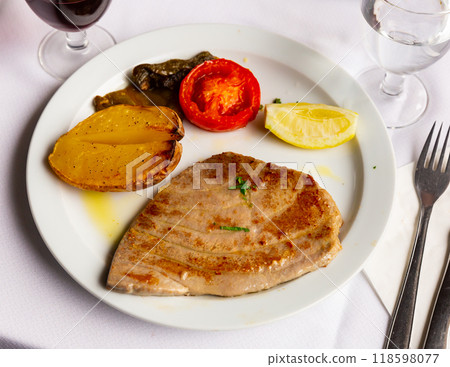 Prepared tuna steak served with lemon and tomato on plate on table Prepared tuna steak served with lemon and tomato on plate on table 118598077