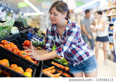Woman choosing tomatoes in fruit and vegetable section of supermarket Woman choosing tomatoes in fruit and vegetable section of supermarket 118598113