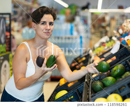 Young Latina choosing ripe avocado on supermarket showcase 118598261
