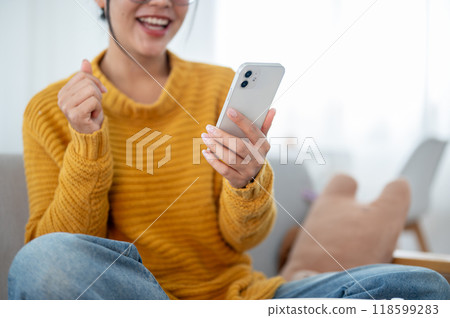 A close-up of a happy woman using her smartphone on a couch in the living room. A close-up of a happy woman using her smartphone on a couch in the living room. 118599283