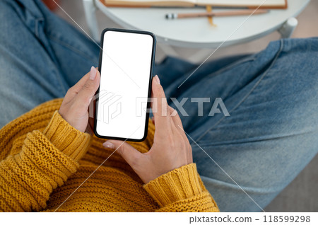 A top view of a woman in casual clothes using her smartphone on a sofa at home. A top view of a woman in casual clothes using her smartphone on a sofa at home. 118599298