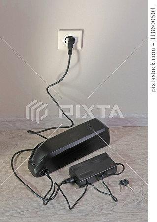 Charging bicycle battery from mains electricity in house. Socket in room with plug switched on. Environmentally friendly transport.  118600501