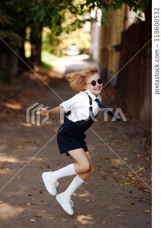 Little girl in school uniform jumping in the air with her hands up. Back to school. 118600532