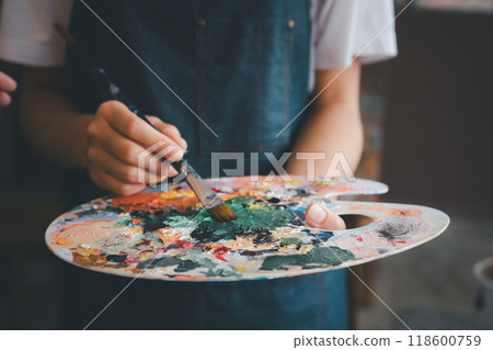 Close-up Art student's hand using a paintbrush to mix colors on a palette in hand to watercolor painting on canvas doing some art projects Close-up Art student's hand using a paintbrush to mix colors on a palette in hand to watercolor painting on canvas doing some art projects 118600759