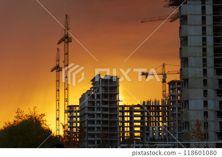 Golden sunset behind a bustling construction site with cranes and buildings silhouetted against the vibrant sky 118601080