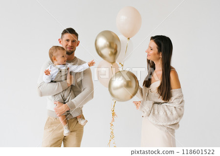 Father and mother are holding a baby and a bunch of balloons. The scene is happy and joyful, as the family is celebrating a special occasion, birthday 118601522