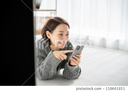 A woman lying down and looking at a smartphone 118601851