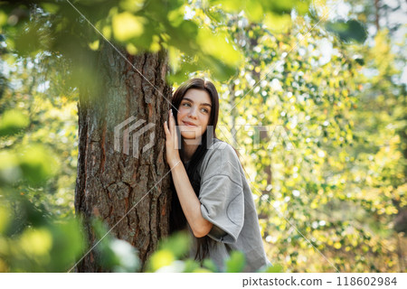 Young woman enjoying a peaceful moment by a tree in a lush green forest during daylight Young woman enjoying a peaceful moment by a tree in a lush green forest during daylight 118602984