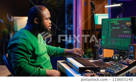 Sound engineer recording piano notes with DAW software in his home studio, working at night on producing new music with electronic tools. Musician composing tunes on midi controller. Camera A. Sound engineer recording piano notes with DAW software in his home studio, working at night on producing new music with electronic tools. Musician composing tunes on midi controller. Camera A. 118603140