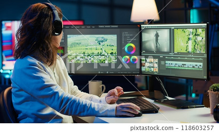 Videographer working on film montage, editing color grading and listening music. Post production studio worker manipulating raw footage, doing adjustments, wearing headphones, camera A Videographer working on film montage, editing color grading and listening music. Post production studio worker manipulating raw footage, doing adjustments, wearing headphones, camera A 118603257