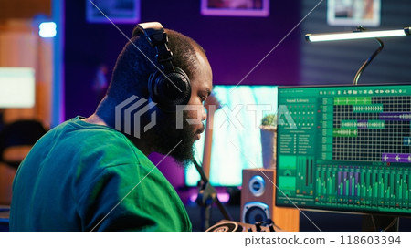 Confident music engineer working on mixing console in home studio, producing new sounds for a song and editing volume levels in daw software. Audio technician recording acoustic files. Camera A. 118603394