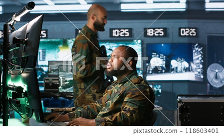 Military agent working in control room, analyzing aerial reconnaissance data and talking with colleague. Intelligence corps agent checking screens, discussing with coworker, camera A Military agent working in control room, analyzing aerial reconnaissance data and talking with colleague. Intelligence corps agent checking screens, discussing with coworker, camera A 118603401
