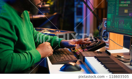 Talented musician creating new soundtracks on mixing console, operating on audio equipment in home studio. Sound technician twisting knobs to edit volume levels on his melody. Camera A. 118603505