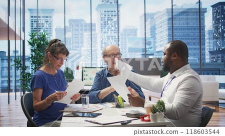 Mature couple meeting with a financial expert to develop a detailed retirement plan, focusing on savings and long term financial security. Clients discussing with broker in office. Camera B. 118603544