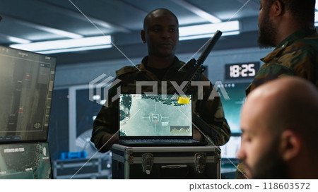 Military soldier wearing camo uniform in mission control center, overseeing national safety operations using laptop. Army expert examining data in monitoring room command center, camera A 118603572