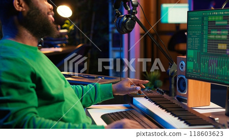 African american artist composing a new soundtrack for a project, using professional production software in home studio. Skilled creative singer producing music and adding sound effects. Camera A. 118603623