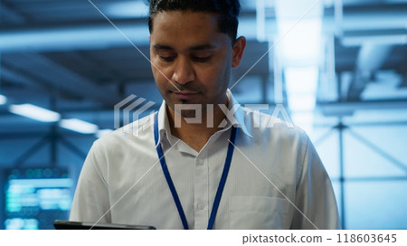 System administrator in data center managing and maintaining databases, ensuring data integrity, security and availability. IT worker updating server room supercomputers systems, camera A System administrator in data center managing and maintaining databases, ensuring data integrity, security and availability. IT worker updating server room supercomputers systems, camera A 118603645