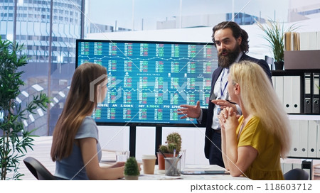 Broker investor in office offering financial advice to clients, looking at stock exchange volatility on big screen. Financial advisor analyzing market shares growth with mother and daughter, camera B 118603712