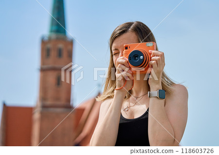 Woman taking photos in European city surrounded by colorful historic buildings. Female tourist captures memories during travel with vintage instant camera 118603726