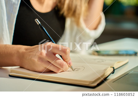 Person is sketching in notebook while working remotely at desk with laptop. Freelance work at home office. Graphic designer drawing sketch Person is sketching in notebook while working remotely at desk with laptop. Freelance work at home office. Graphic designer drawing sketch 118603852