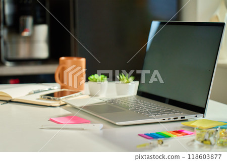 Minimalist home office with laptop, small potted plants and coffee mug on white desk with kitchen interior in background. Workspace for distant work from home Minimalist home office with laptop, small potted plants and coffee mug on white desk with kitchen interior in background. Workspace for distant work from home 118603877