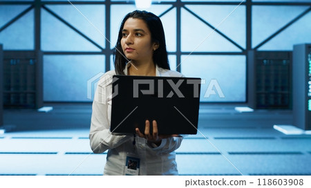 Programmer walking in data center, using notebook to design, implement and manage gear, ensuring optimal performance and reliability. IT professional in server hub coding on laptop, camera A 118603908