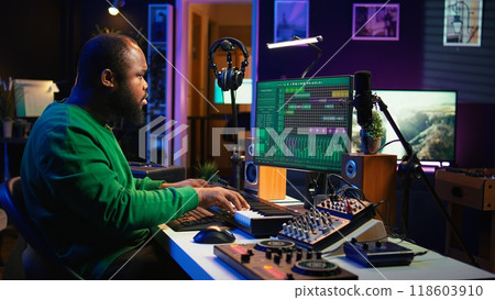Producer composing new track with electronic gear in his home studio, creating music on mixing console and software interface. Talented artist songwriter controls panel to produce sounds. Camera B. 118603910