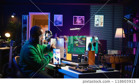 Artist pointing at musical sheet notation to explain notes on piano, teaching people to play synthesizer in home studio. Composer musician playing midi controller during online master class. Camera B. 118603915