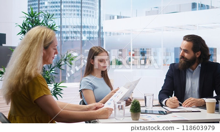 Financial adviser providing clients with informative leaflets on retirement planning, tax issues and wealth management. Agent in office assisting clients in setting up investment accounts, camera A 118603979