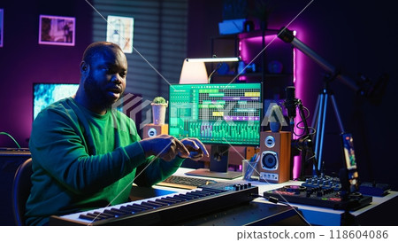 Musician doing online paid classes to help people play piano notes, teaching lessons from his home studio and recording video tutorials. Musical instructor playing midi controller keyboard. Camera B. Musician doing online paid classes to help people play piano notes, teaching lessons from his home studio and recording video tutorials. Musical instructor playing midi controller keyboard. Camera B. 118604086