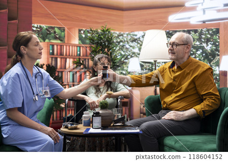 Medical assistant preparing daily dose of pills and vitamins for elderly patients, dividing the medicaments in separate bottles for effectiveness. Nurse giving medical drugs to people. 118604152