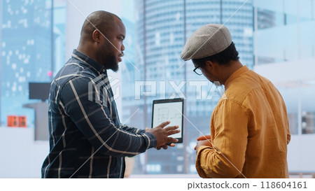 Real estate broker and client negotiating a leasing contract for a high class modern office space, evaluating blueprints on tablet during office tour. Property investment opportunity. Camera B. Real estate broker and client negotiating a leasing contract for a high class modern office space, evaluating blueprints on tablet during office tour. Property investment opportunity. Camera B. 118604161