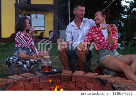 Family mom, dad, daughter are drinking tea in the courtyard of the house by the fire pit on a cozy summer evening. Family mom, dad, daughter are drinking tea in the courtyard of the house by the fire pit on a cozy summer evening. 118604191
