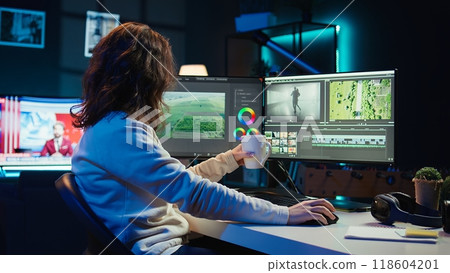 Videographer using editing software to assemble footage into cohesive final result while enjoying cup of coffee. Specialist color correcting clips while drinking hot beverage, camera B 118604201