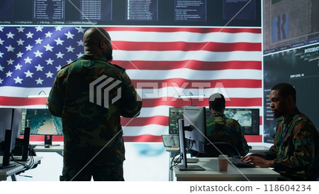 Team of military experts operates high tech computers and tablet to analyze surveillance data and manage national security operations. Working with CCTV radar satellite imagery. Camera B. 118604234