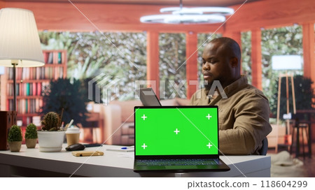 Small business owner works on finances plans next to a green screen, using annual sales analytics to increase startup profit. Entrepreneur does budget balance analysis at home desk. Camera B. 118604299