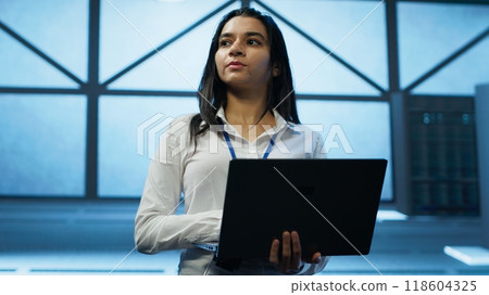 Admin in data center managing servers, operating systems and software programs. Tracking shot of woman in server hub ensuring networks are secure, up to date, and functioning properly, camera A 118604325