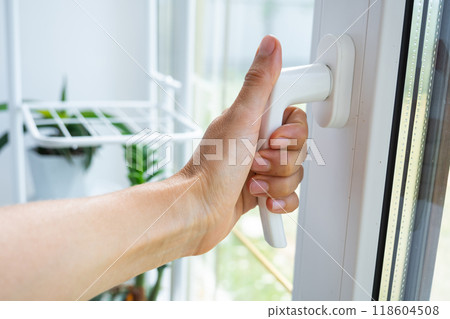 The hand holds the handle of a plastic double-glazed window, closing and opening the window with a rotary mechanism, the position of the handle for ventilation, micro-ventilation 118604508