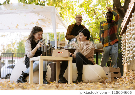 Shopping at an organic food festival, a young woman sits at a table with a local winemaker and tastes homemade natural wine before making a purchase. People sampling products at the farmers market. Shopping at an organic food festival, a young woman sits at a table with a local winemaker and tastes homemade natural wine before making a purchase. People sampling products at the farmers market. 118604606