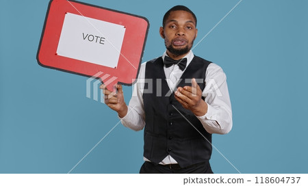 Hospitality industry worker shows speech bubble with political message, urging people to vote with cardboard sign advertisement. Hotel porter employee holds icon with commercial ad. Camera B. 118604737