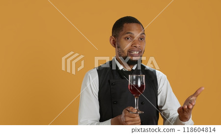 Restaurant employee bringing a glass of red wine to clients at the table, serving people at a five star diner. Waiter with professionalism focusing on customer satisfaction. Camera A. Restaurant employee bringing a glass of red wine to clients at the table, serving people at a five star diner. Waiter with professionalism focusing on customer satisfaction. Camera A. 118604814